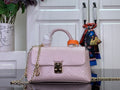 Light pink textured leather handbag with orange top handle, gold chain strap and front clasp.
