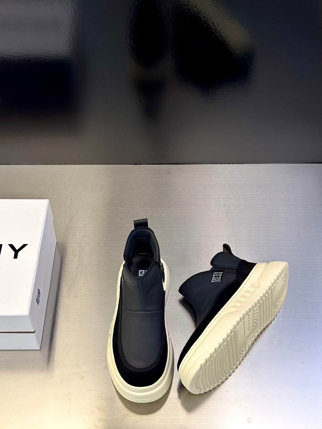 Side-by-side pair of dark and light mid-top slip-on sneakers with thick cream soles.