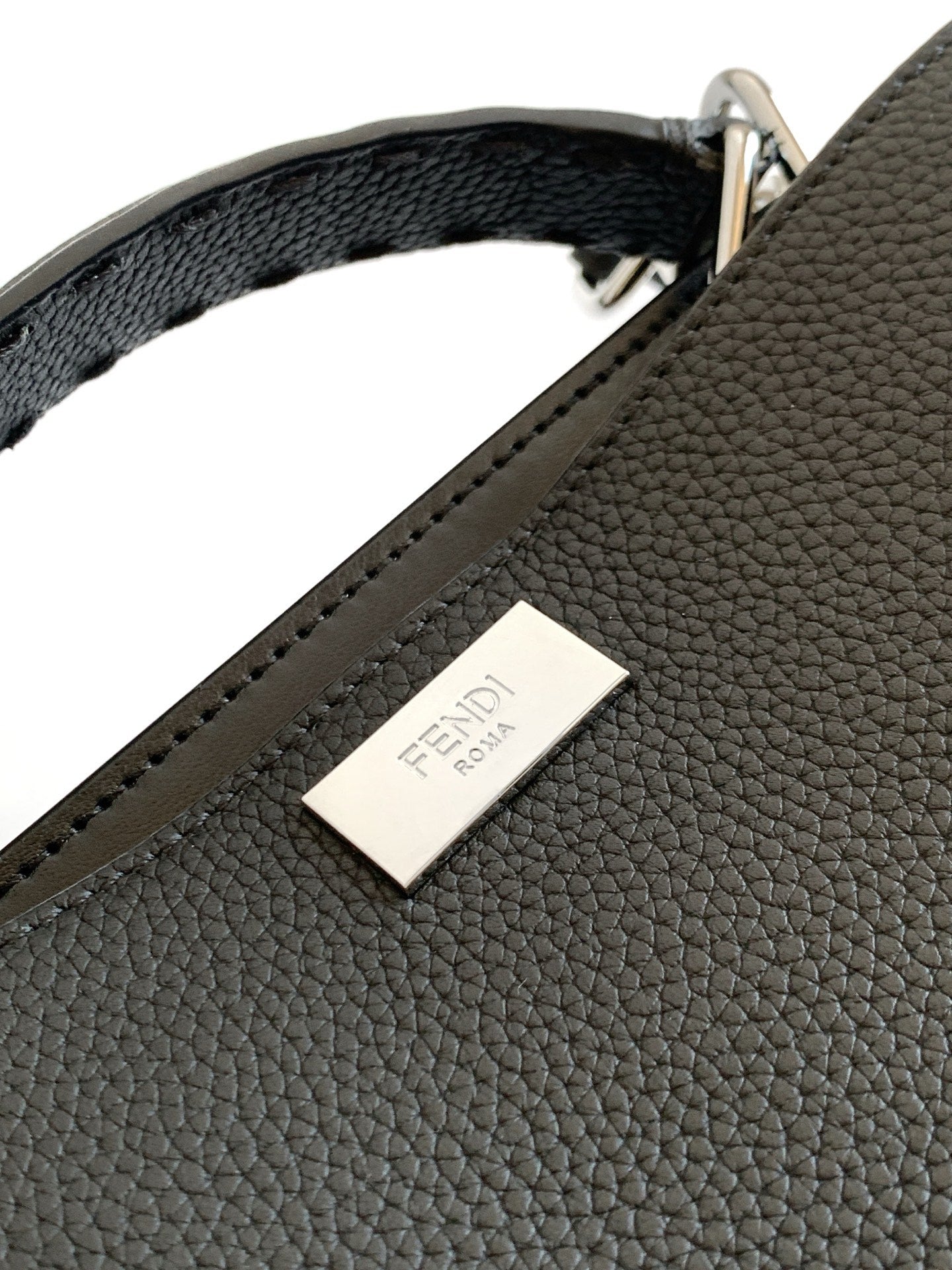 Fendi leather handbag label on pebbled black exterior with stitched edge.