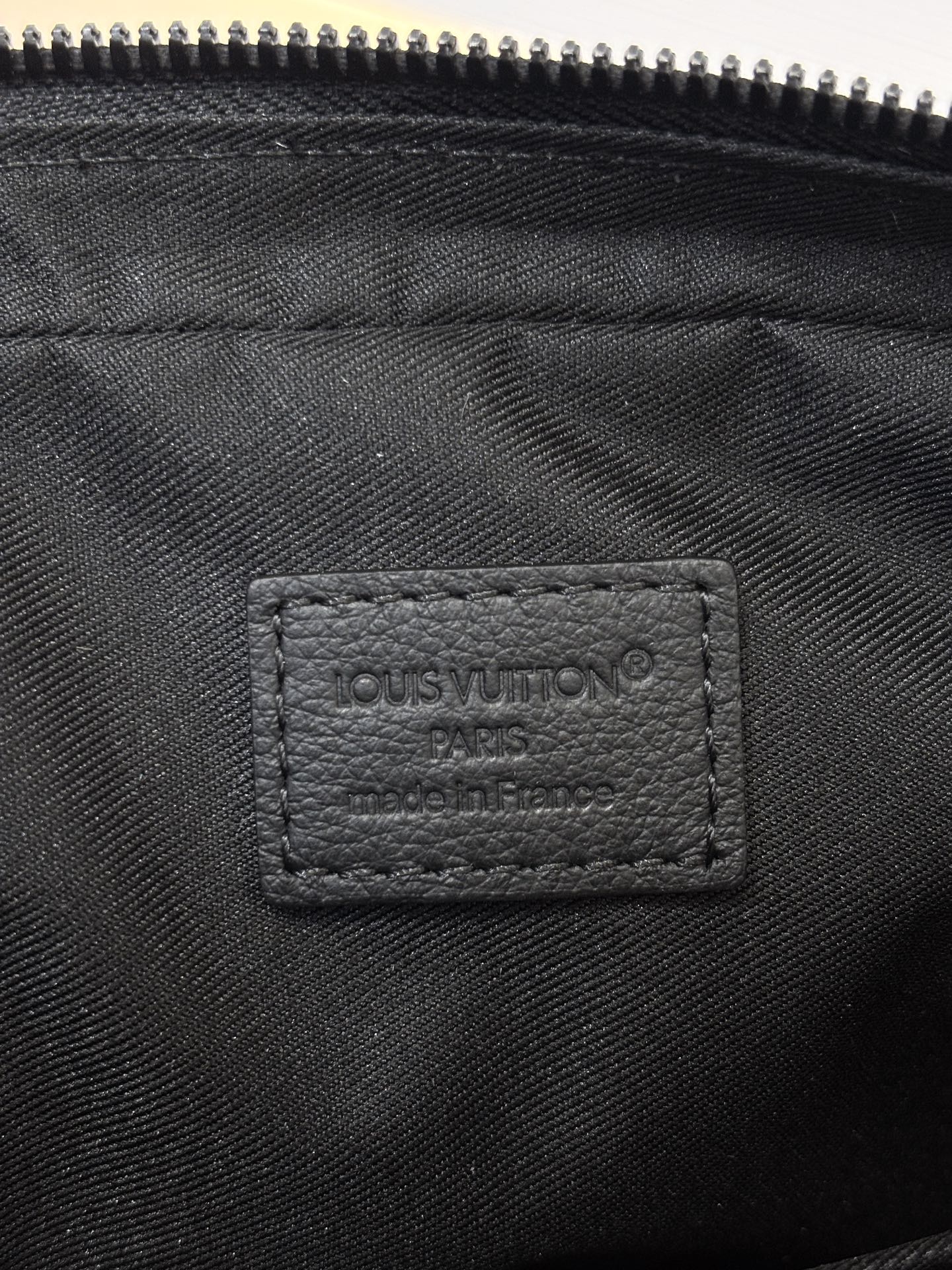 Louis Vuitton black monogram bag close-up of inner label under zipper opening