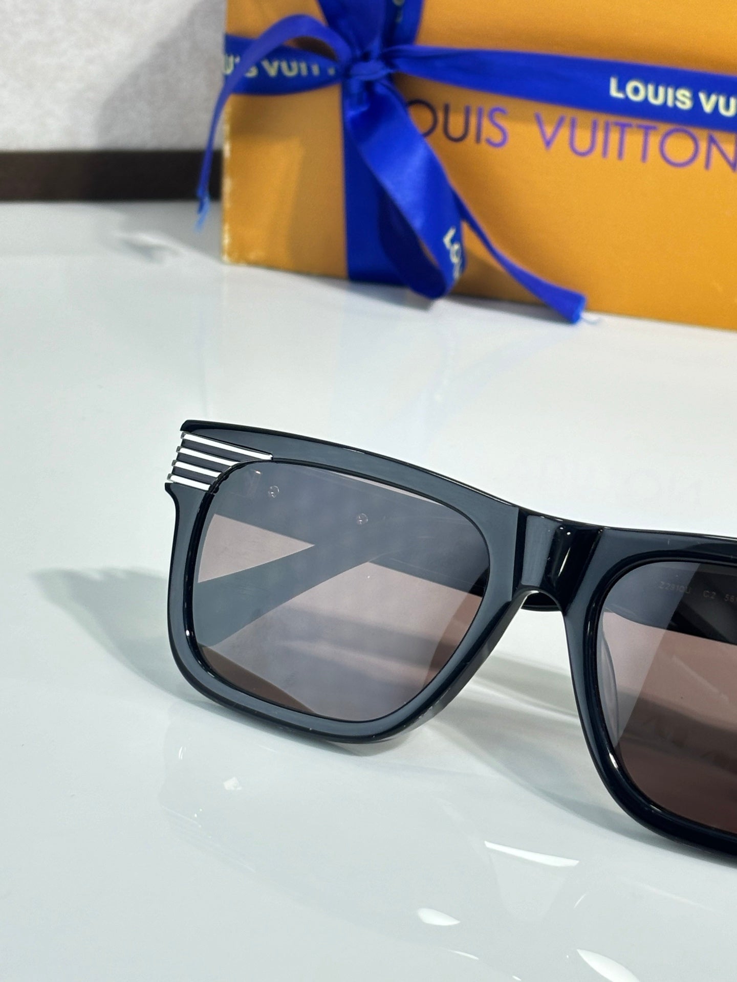 Close-up black eyeglasses with tinted lenses and striped LV detailing on the frame.