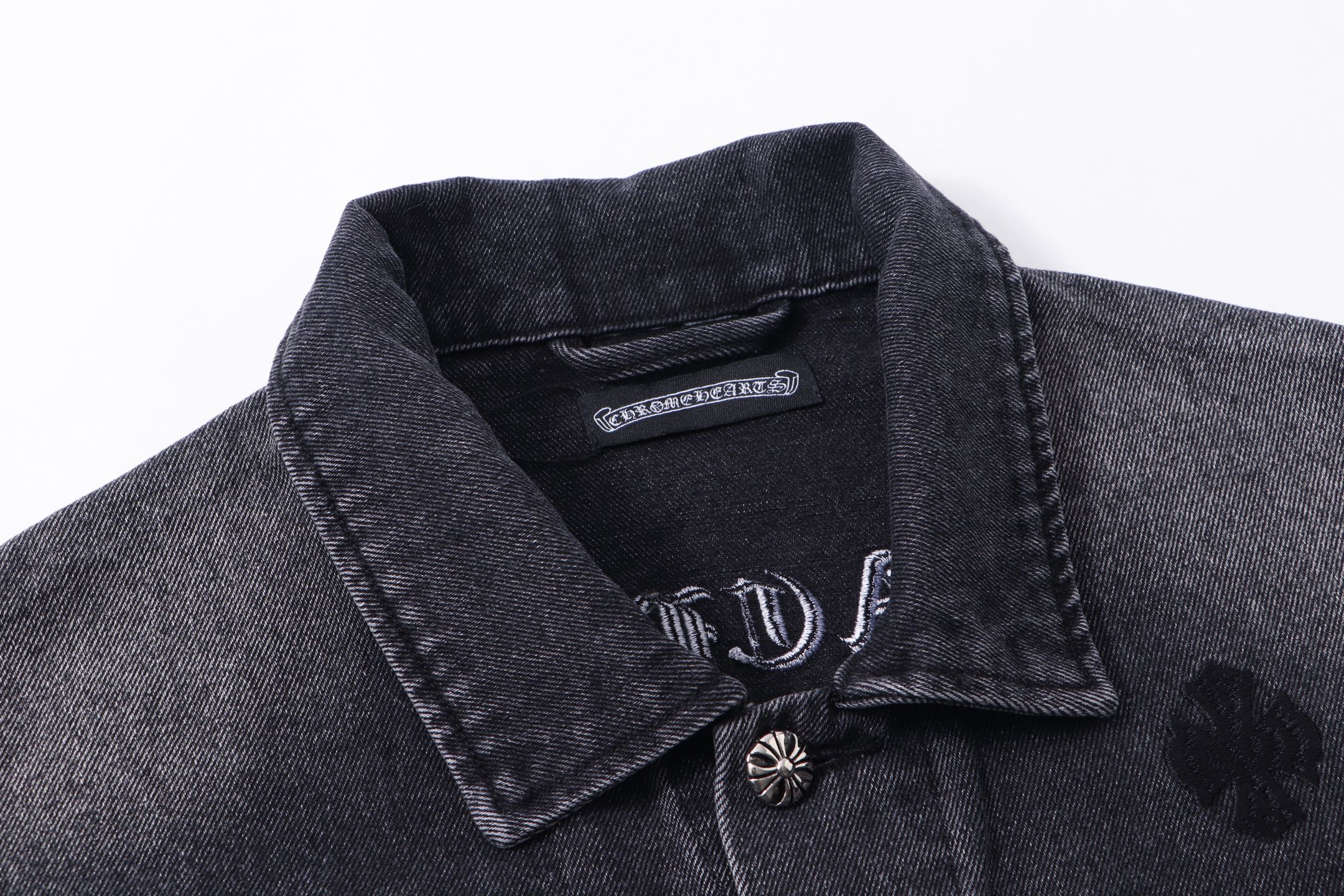 Dark denim jacket collar with snap buttons and small embroidered emblem
