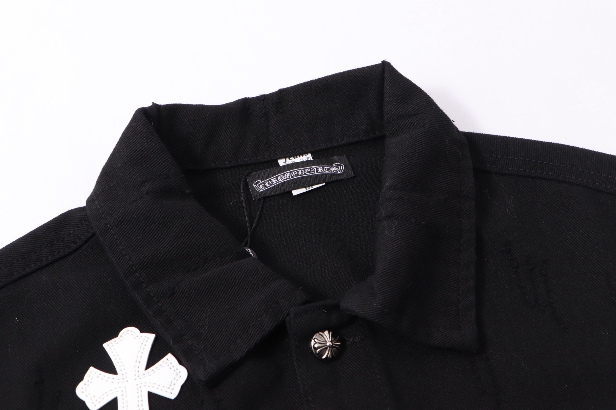 Black denim jacket neckline close-up with inner label and white cross patch
