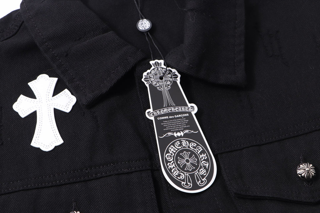 Black denim jacket close-up at collar with white cross patch and hanging tag