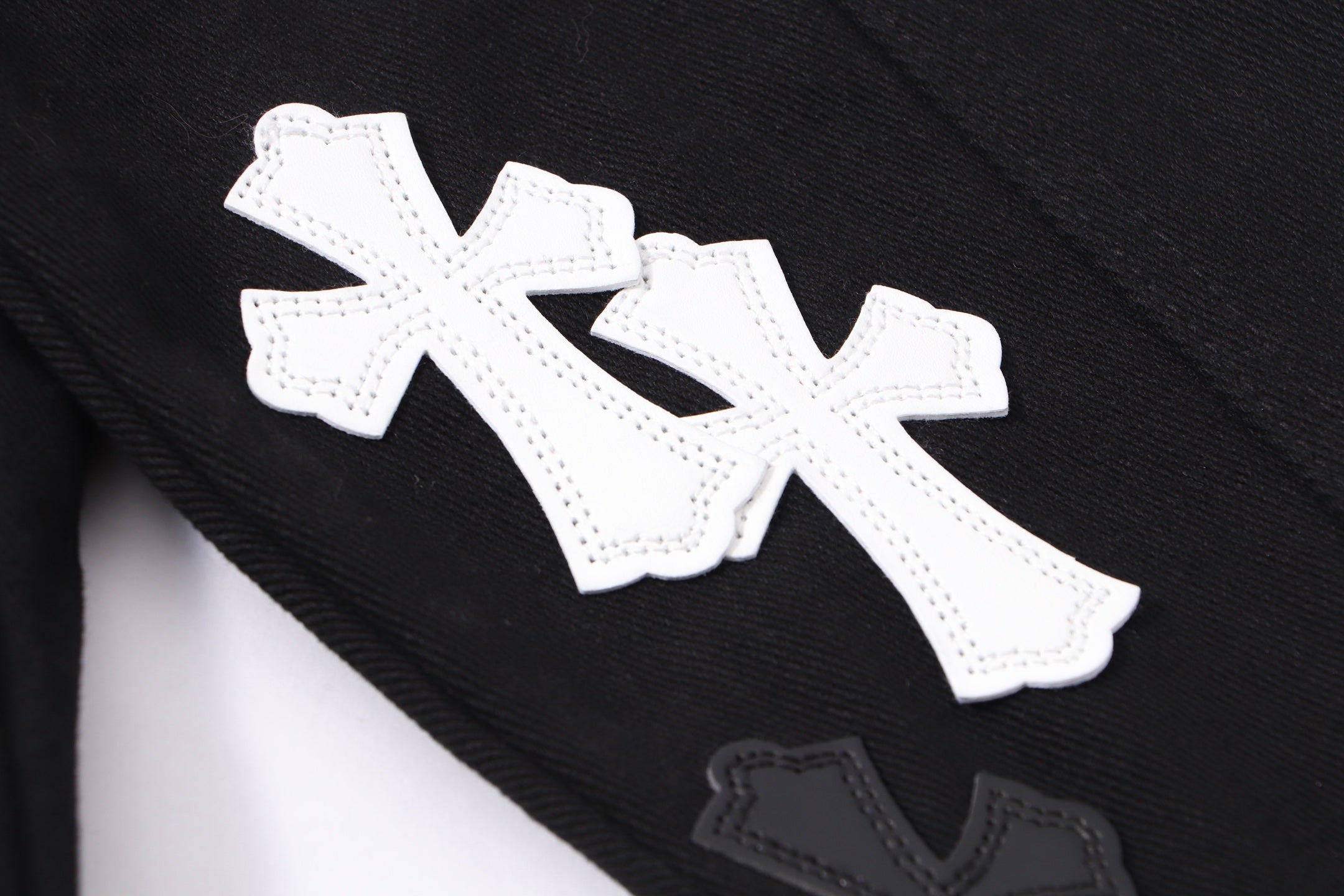 Black denim jacket sleeve detail with large white cross applique and stitched edges