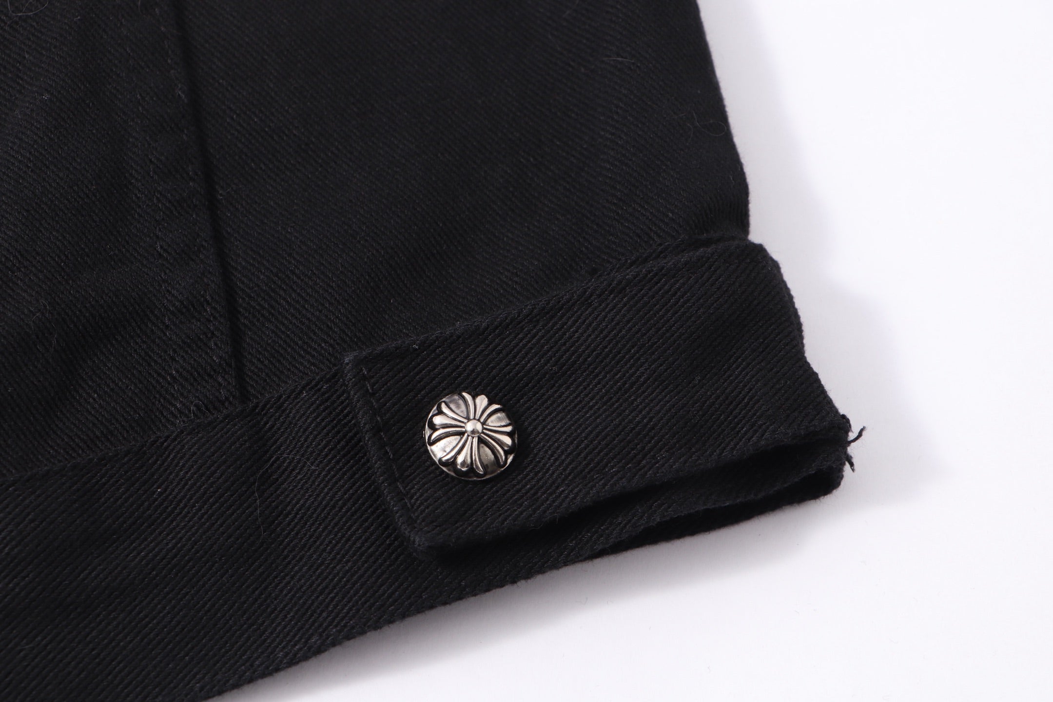 Black denim jacket cuff with metallic snap and folded hem
