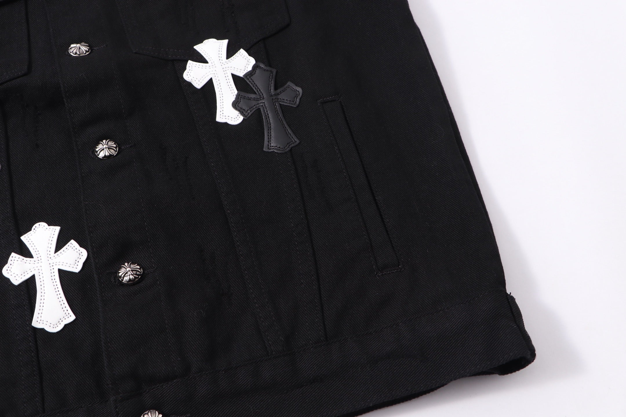 Black denim jacket lower front detail with white cross patch and snap buttons
