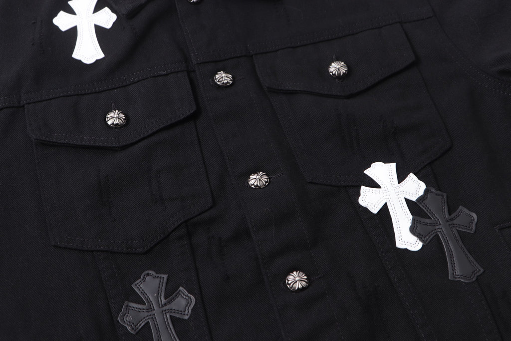Black denim jacket front close-up with flap pockets, snaps, and cross appliques
