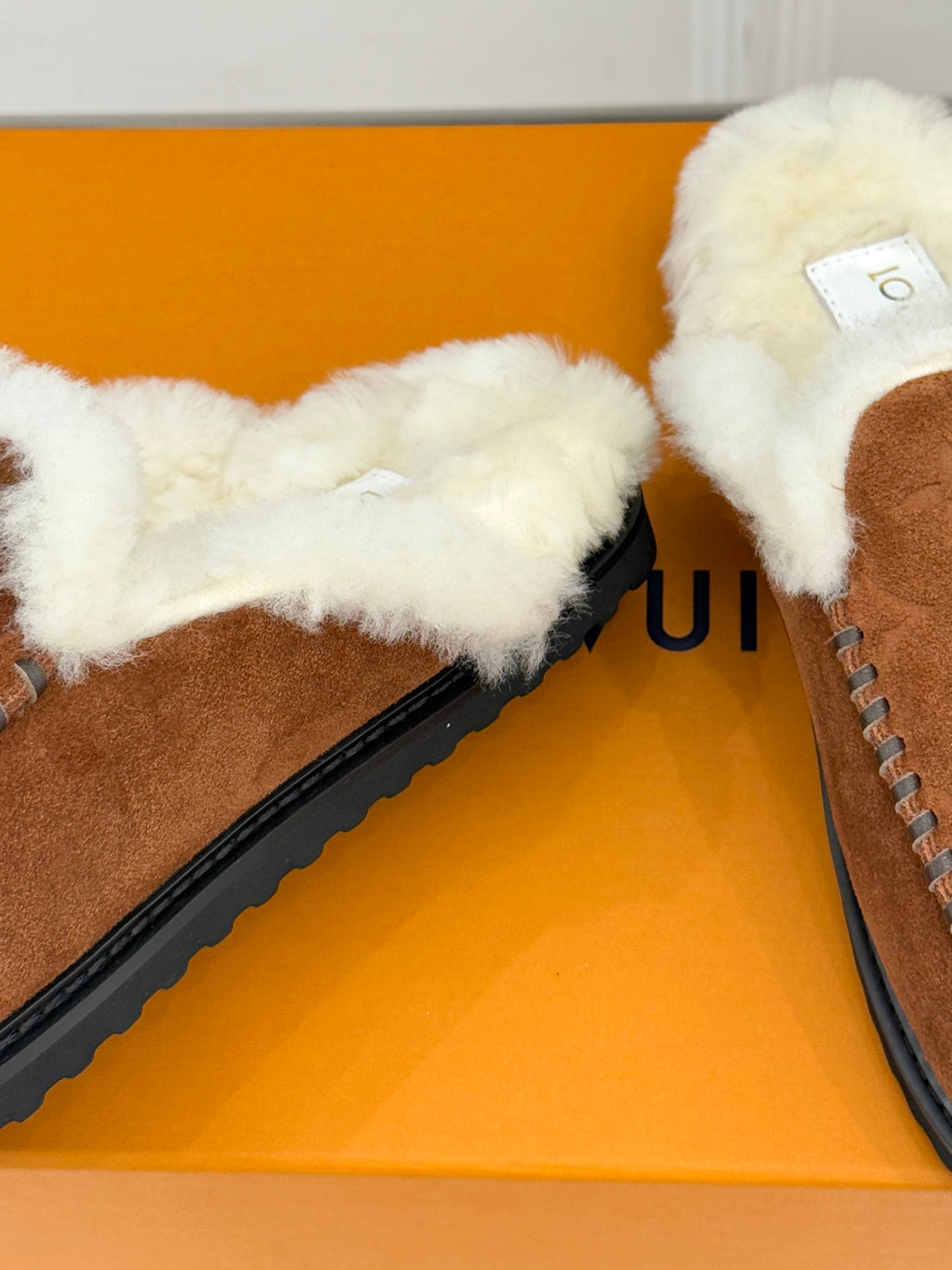 Brown suede slipper loafer with white shearling trim and visible inner label