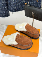 Two brown suede slip-on loafers with white shearling trim and embossed logo details