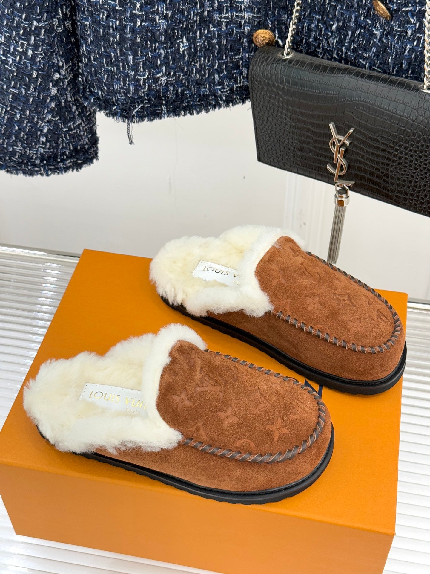 Two brown suede slip-on loafers with white shearling trim and embossed logo details