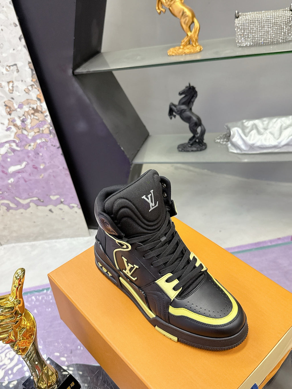Black high-top sneakers with neon yellow edging, displayed on orange box