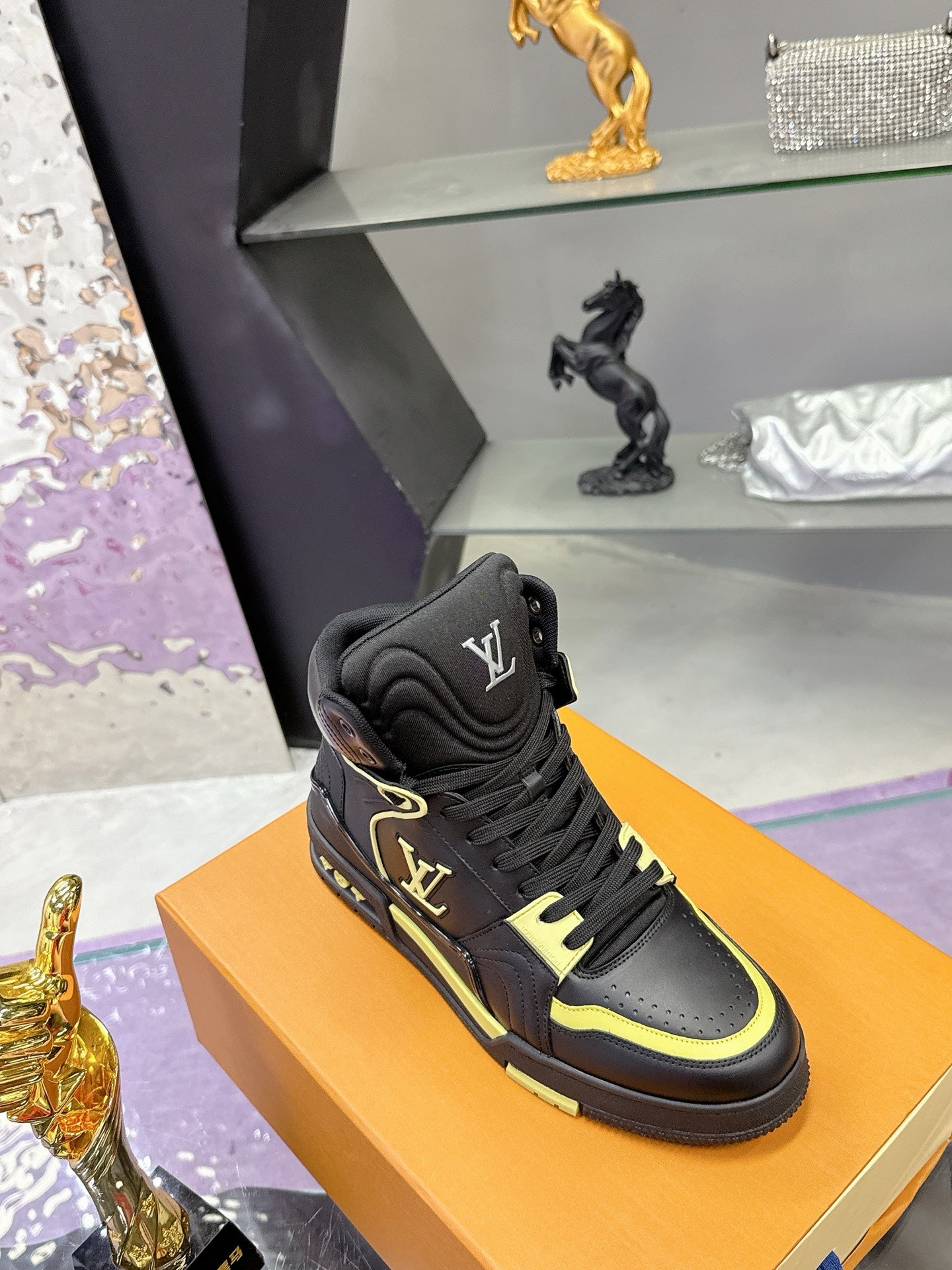 Black high-top sneakers with neon yellow edging, displayed on orange box