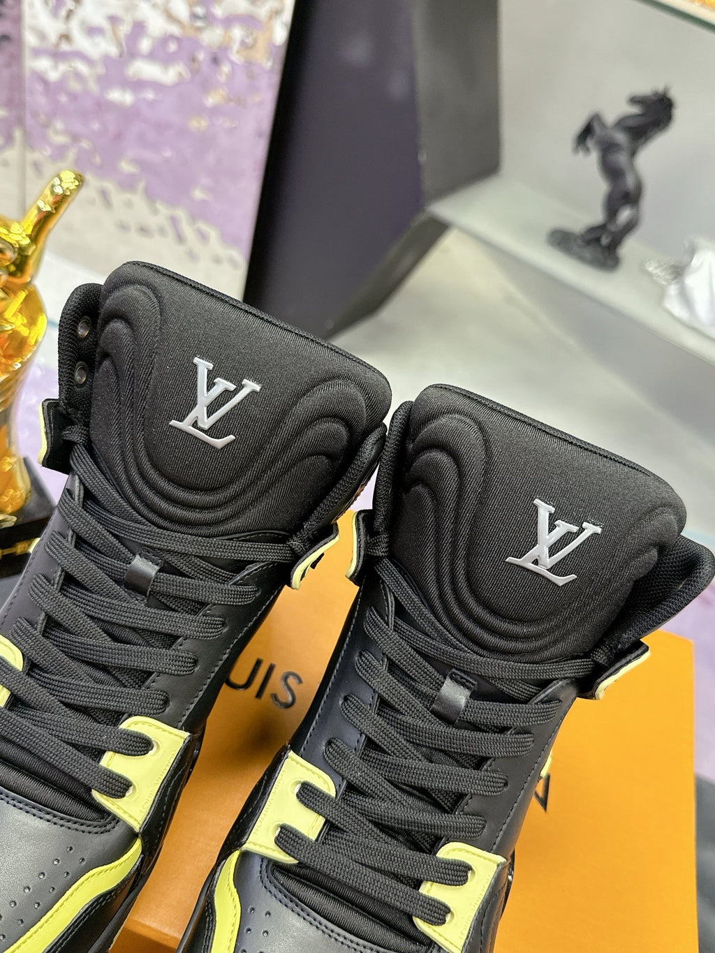 Black high-top sneakers detail view: LV logo patch and neon yellow trim