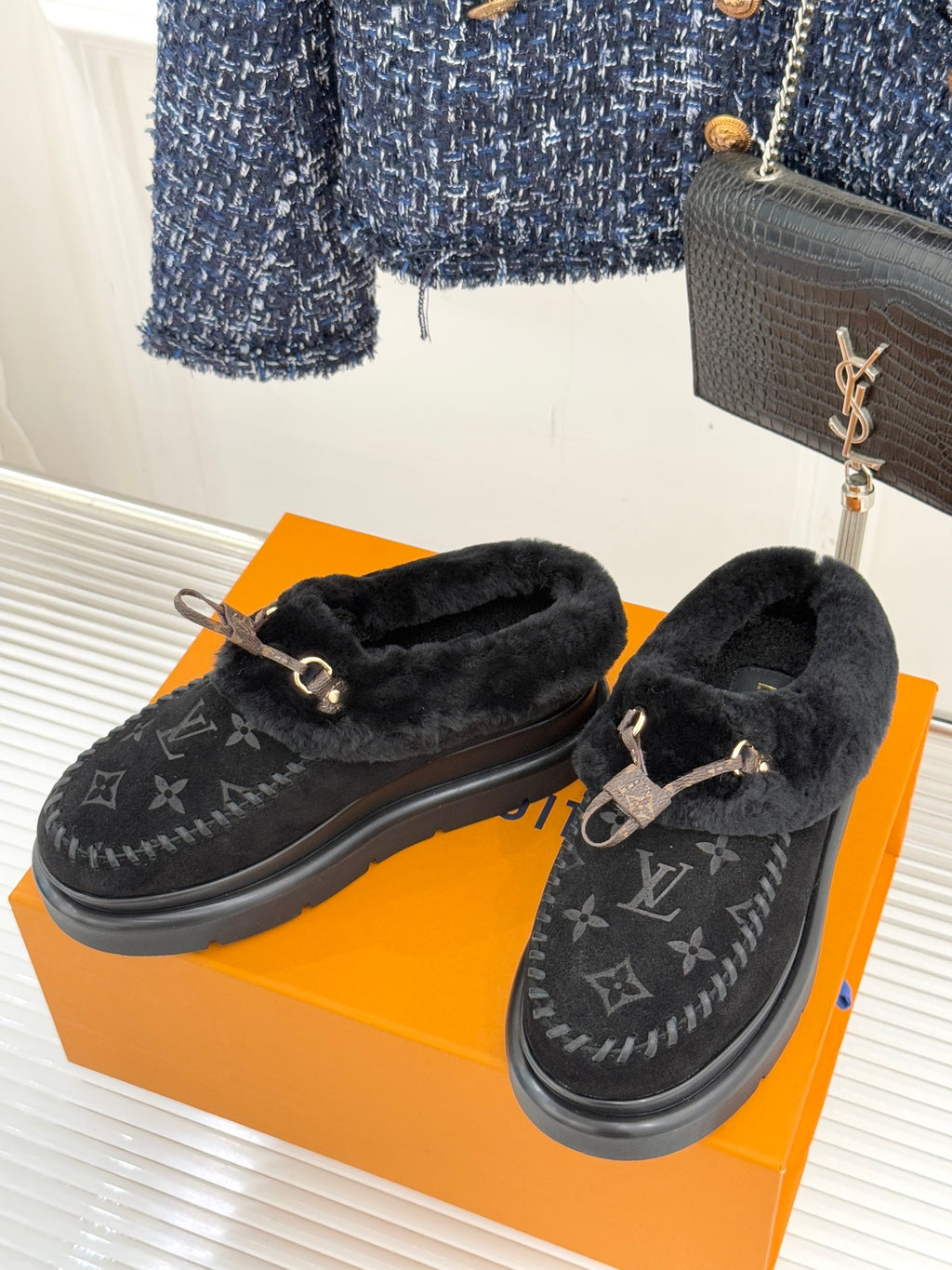 Black shearling loafers with monogram upper and gold-tone buckle, pair on an orange box