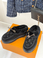 Black shearling loafers with monogram upper and gold-tone buckle, pair on an orange box