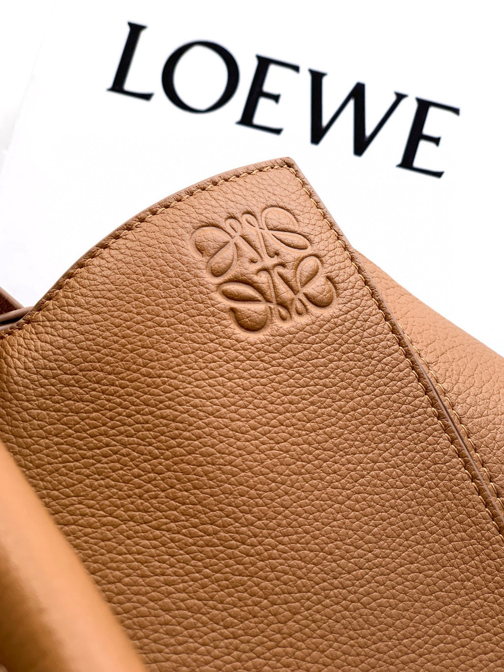 Tan leather bag panel with embossed logo and textured grain finish.