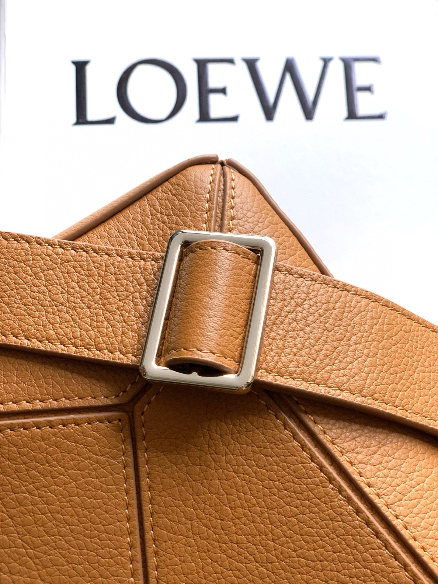 Tan leather belt-style strap with metal buckle attachment and stitched edges.