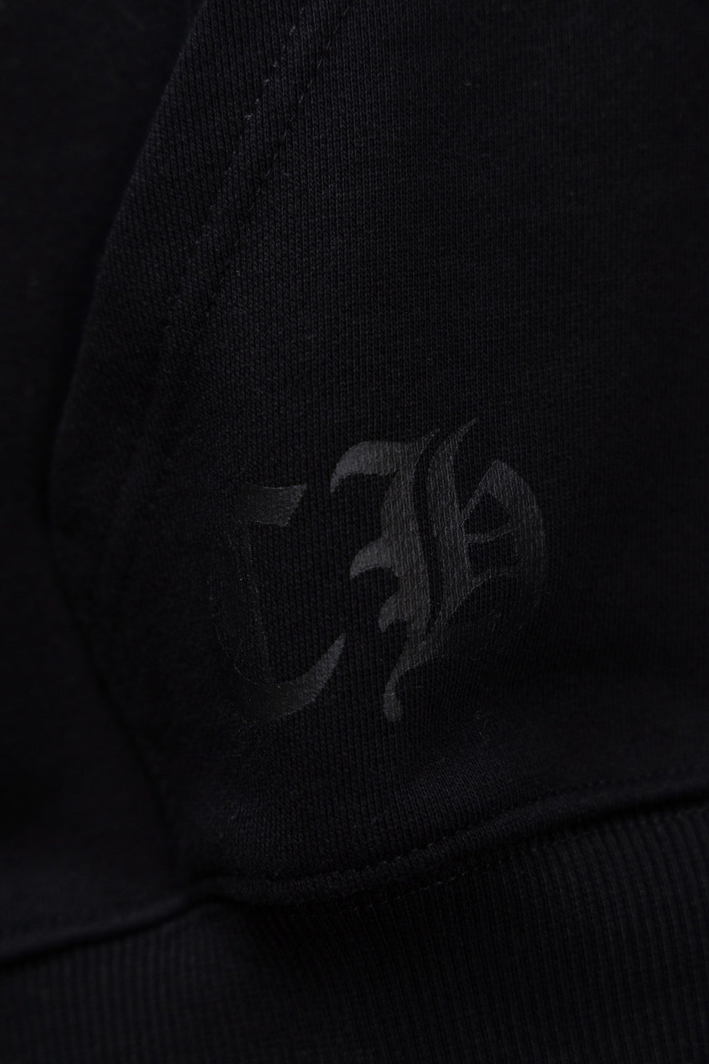 Black hoodie fabric with faint dark emblem detail