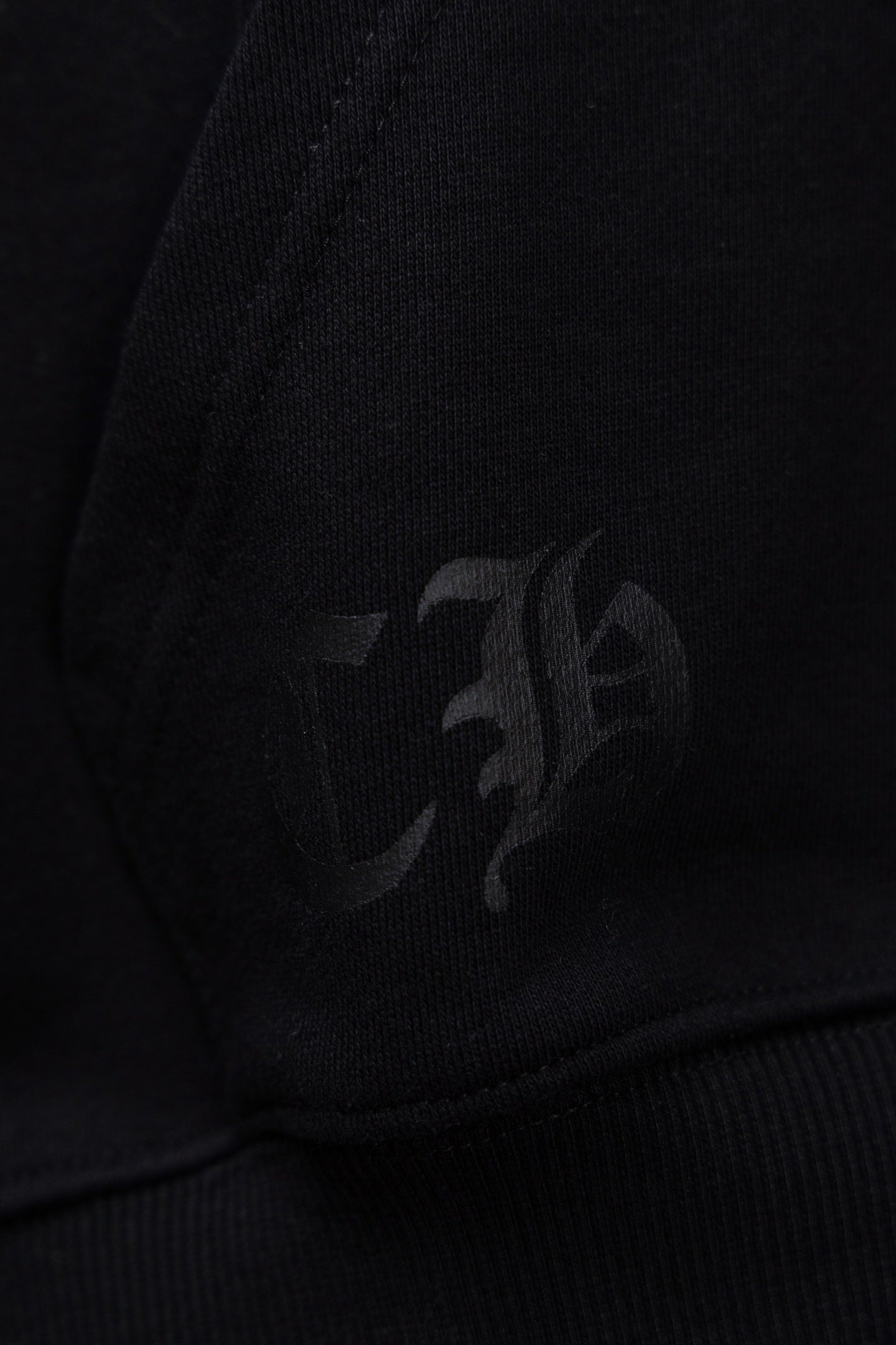 Black hoodie fabric with faint dark emblem detail