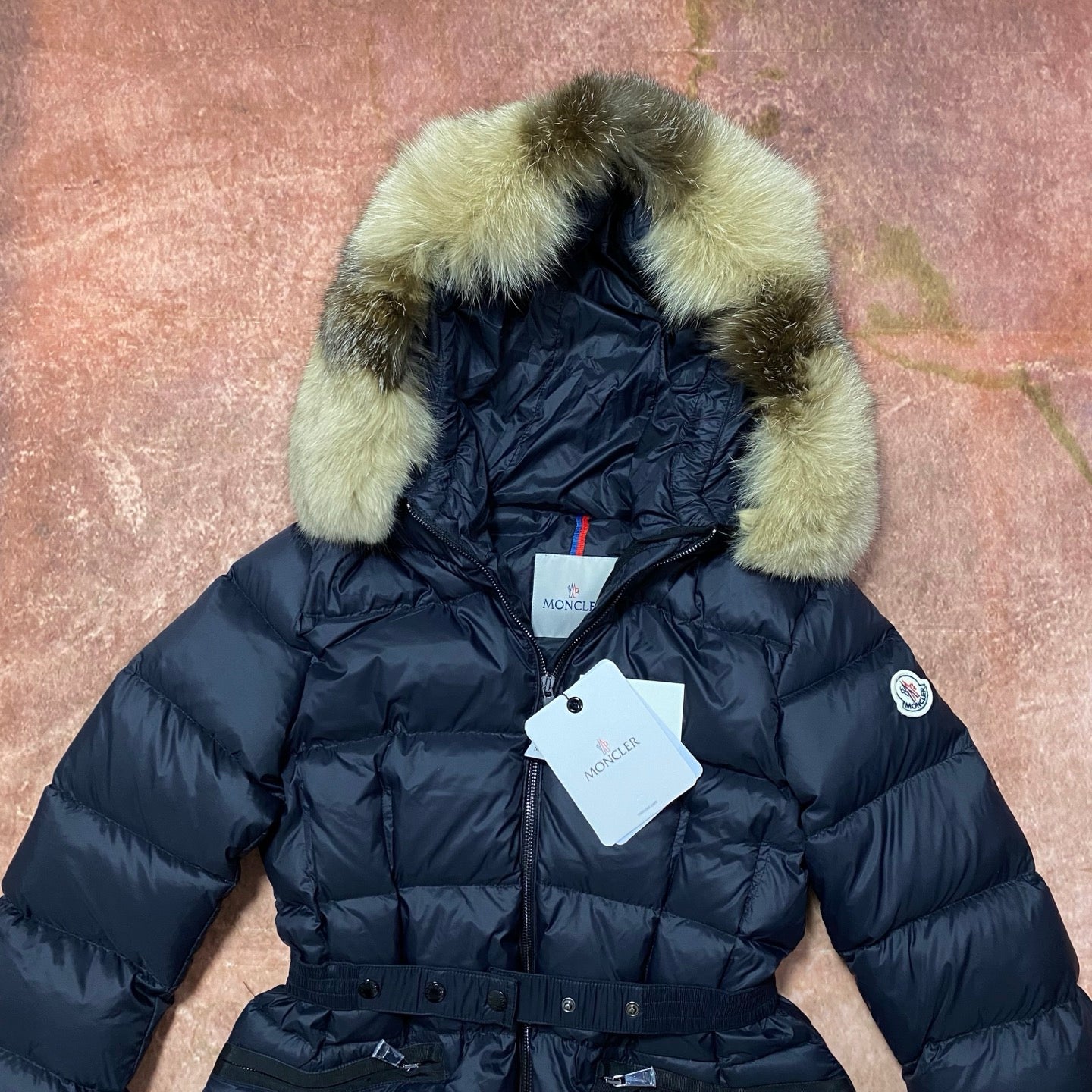 Long navy puffer coat with green faux-fur hood, zip front, logo patch and tags