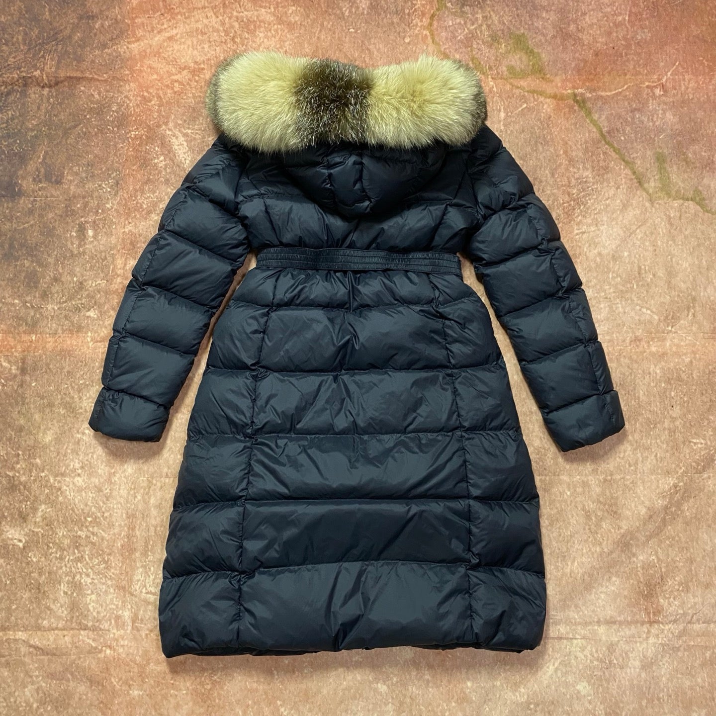 Long navy puffer coat with green faux-fur hood and belted waist, zip front