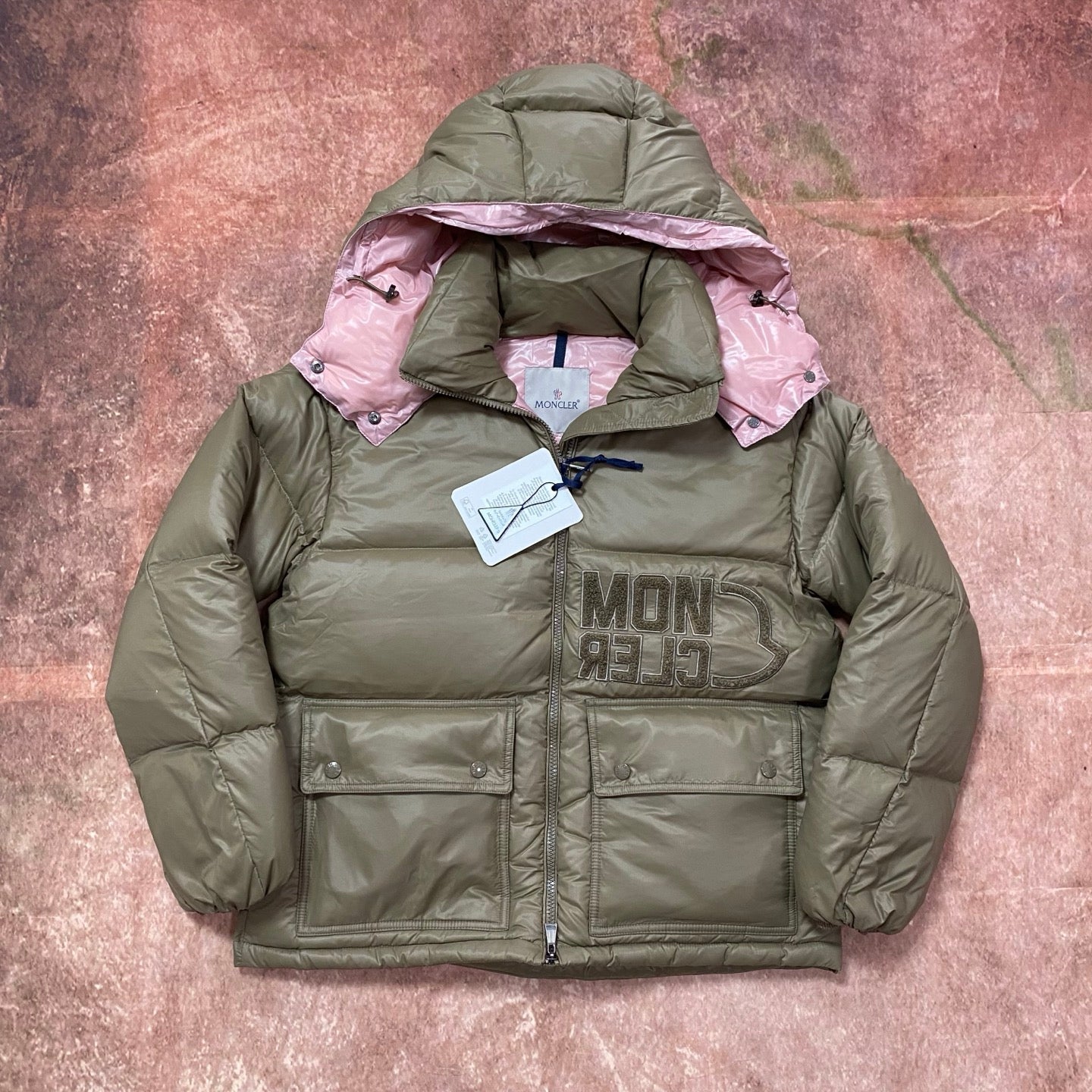 Olive green long puffer jacket with pink hood lining, quilted front and snap pockets.