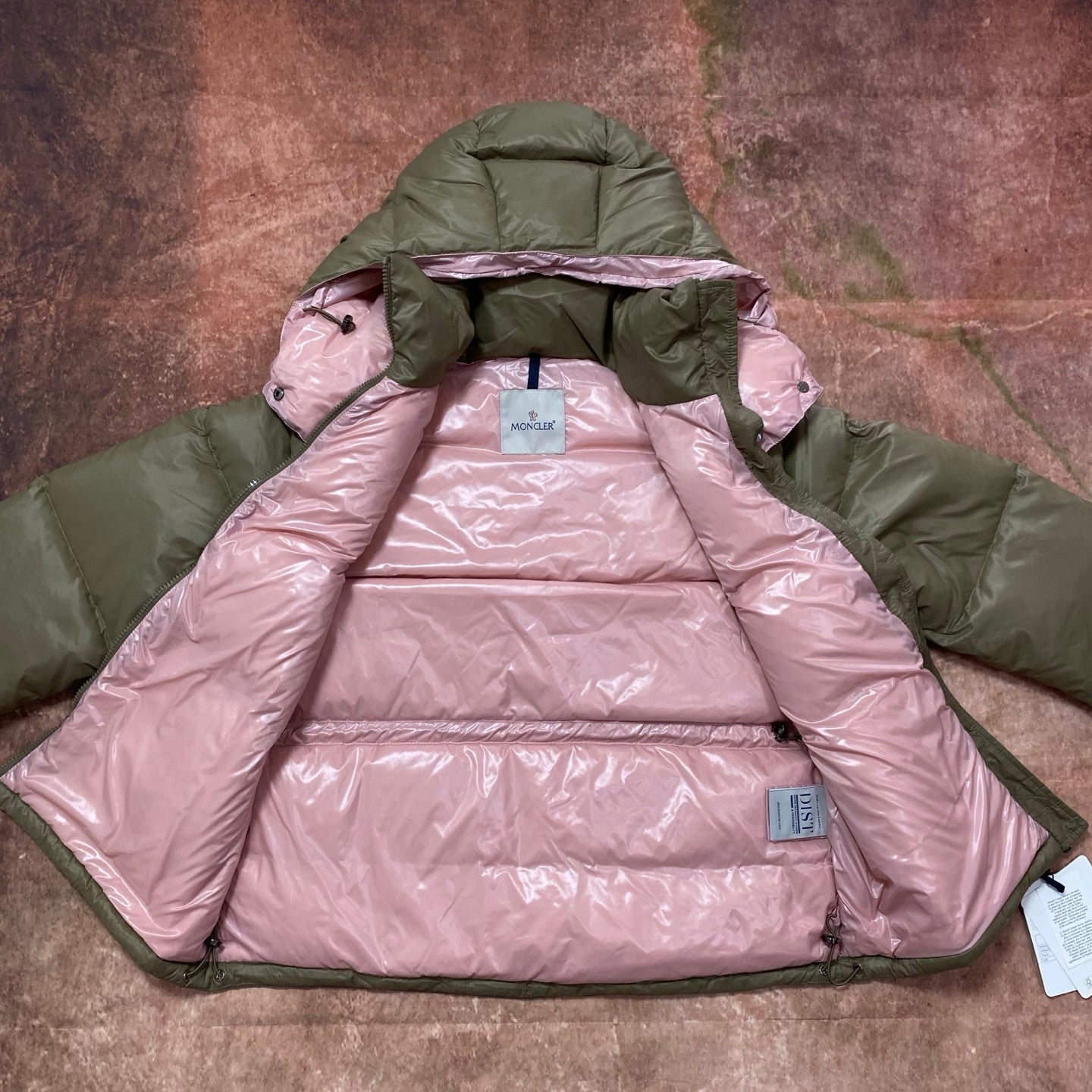Olive green and pink hooded puffer jacket, showing pink insulated lining and hood.