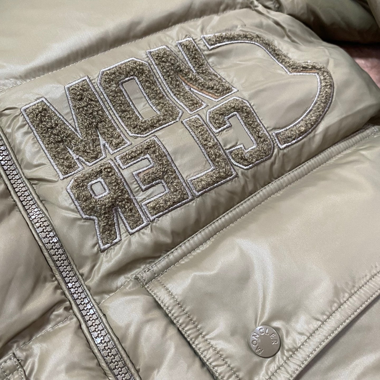 Olive green puffer jacket with raised metallic logo lettering on chest panel.
