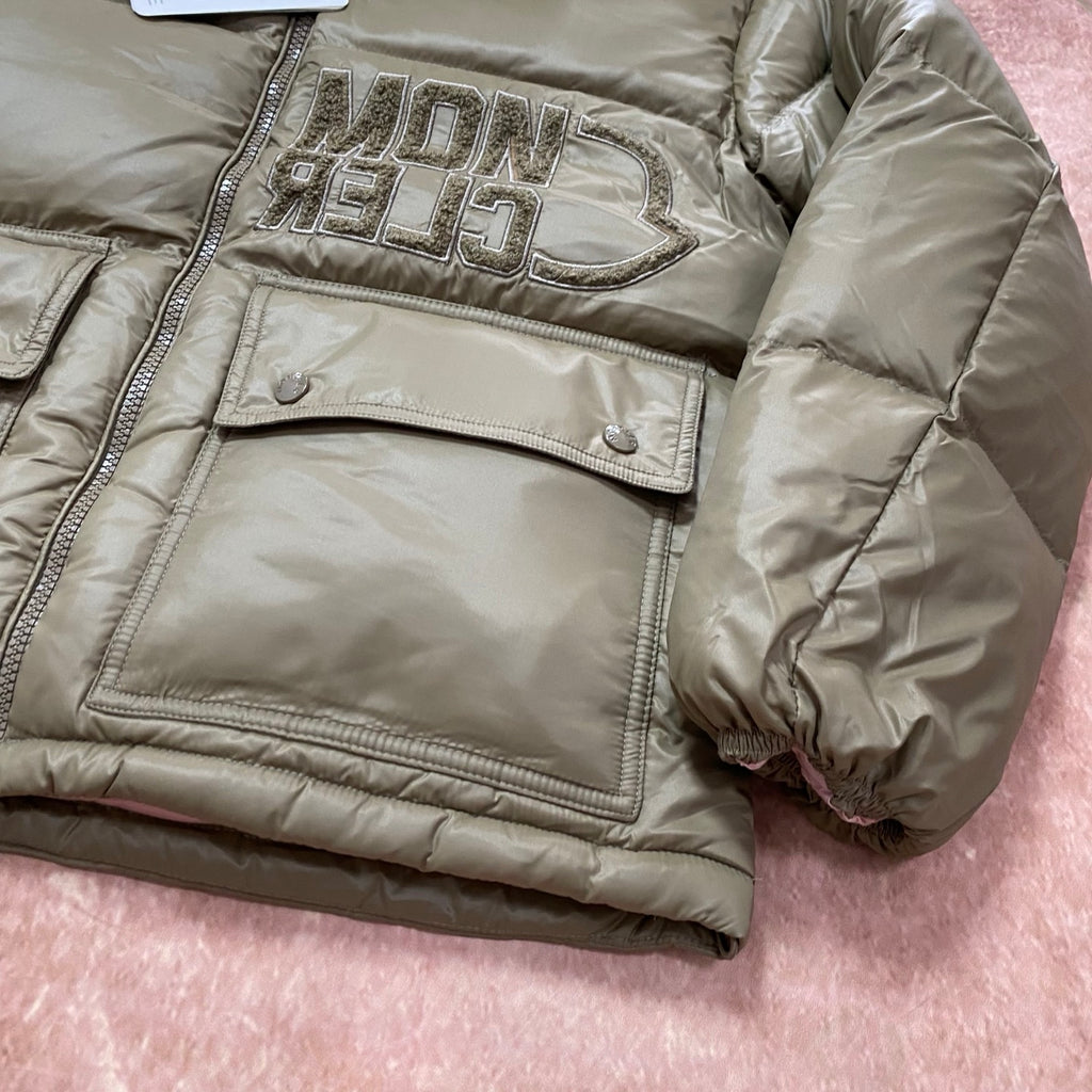Olive green puffer jacket with large metallic logo patch and flap pocket detail.