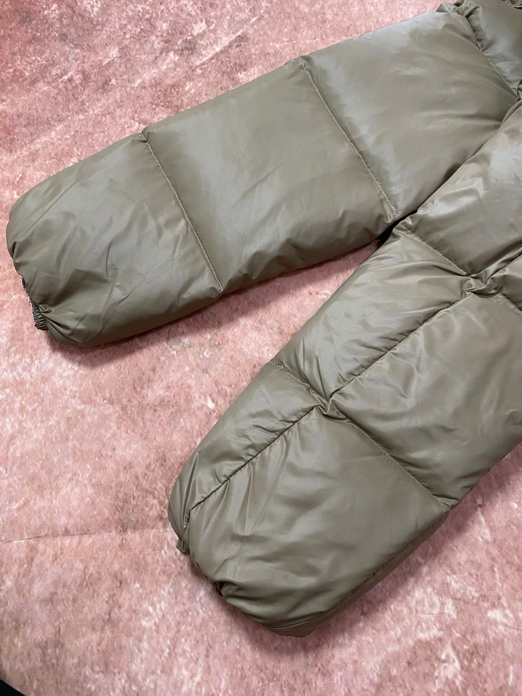 Olive green long puffer jacket sleeves and hem, padded quilted construction on display.