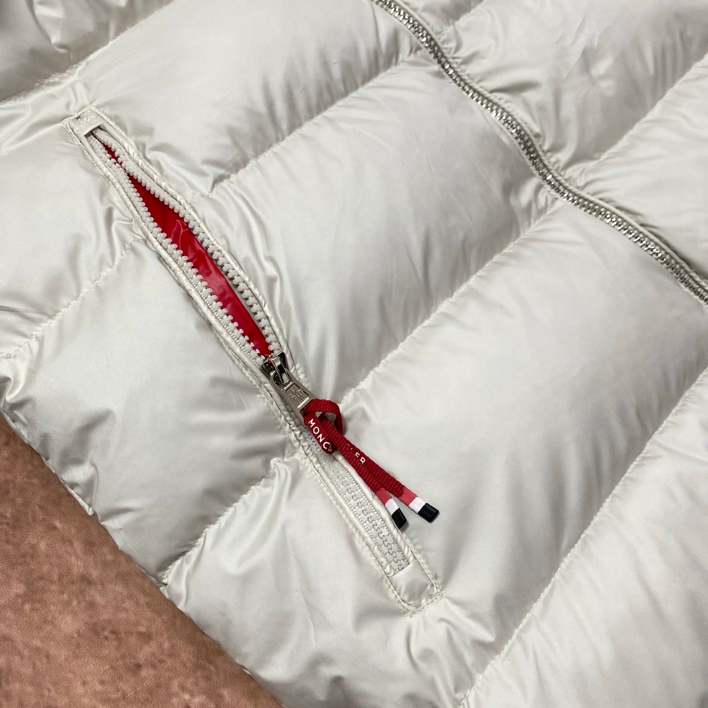 Moncler cream puffer jacket front zipper with red-trim pull and metal zipper teeth