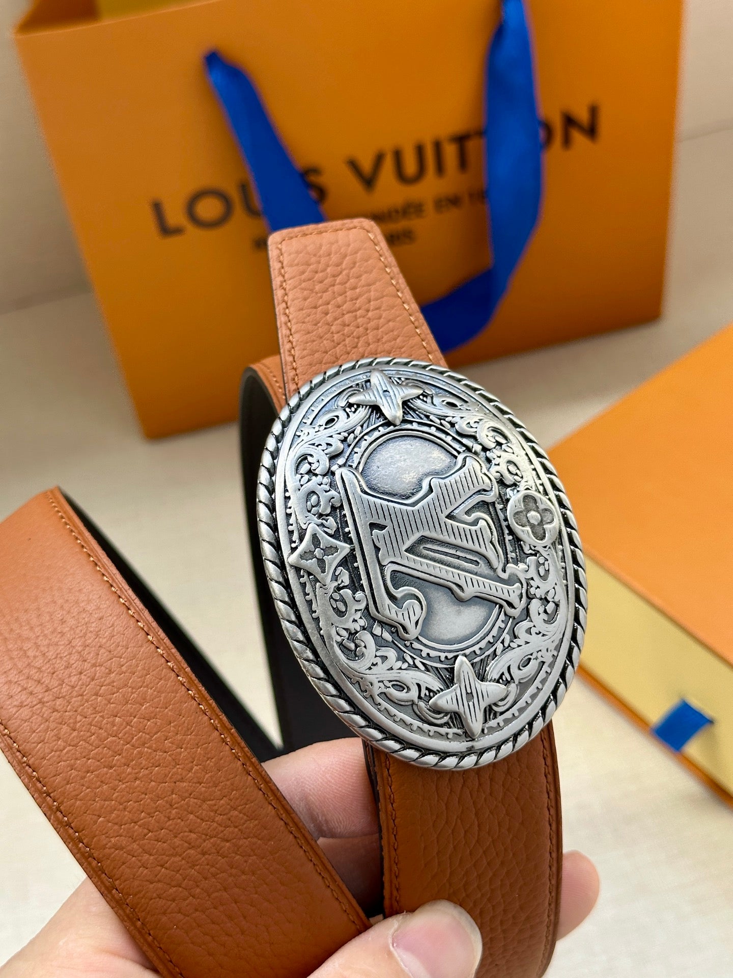Louis Vuitton belt buckle close-up: silver oval logo on tan leather strap