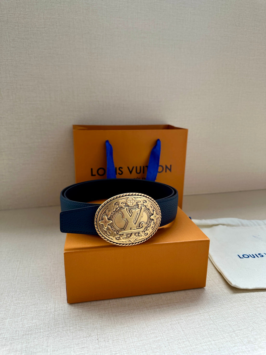 Blue leather belt with gold oval buckle resting on orange gift boxes