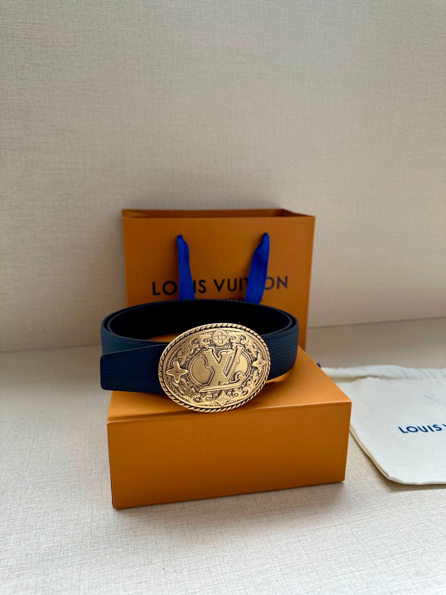 Blue leather belt with gold oval buckle resting on orange gift boxes