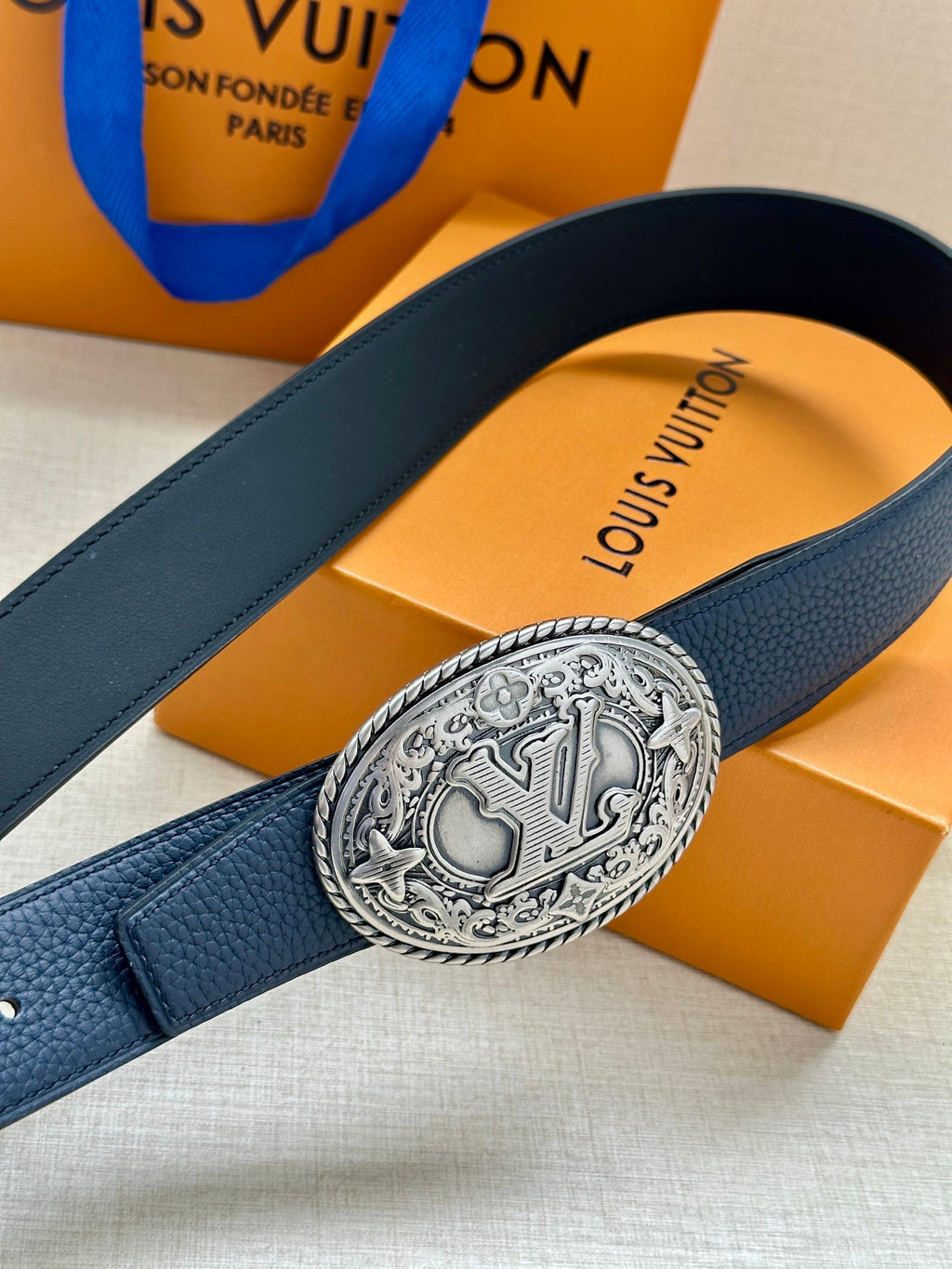 Navy leather belt detail with embossed oval silver buckle and stitched strap
