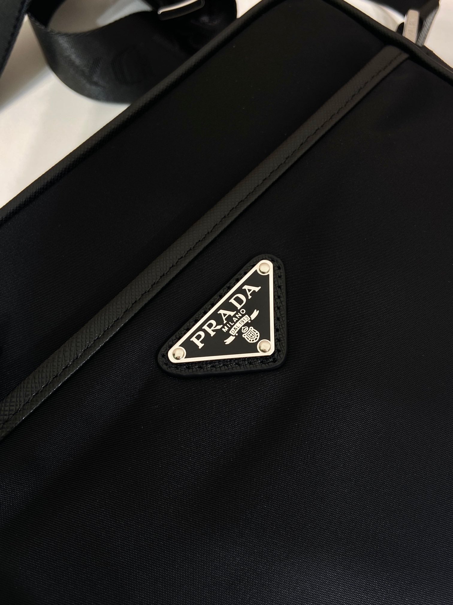 Leather strap with Prada logo patch and metal buckle on dark blue bag