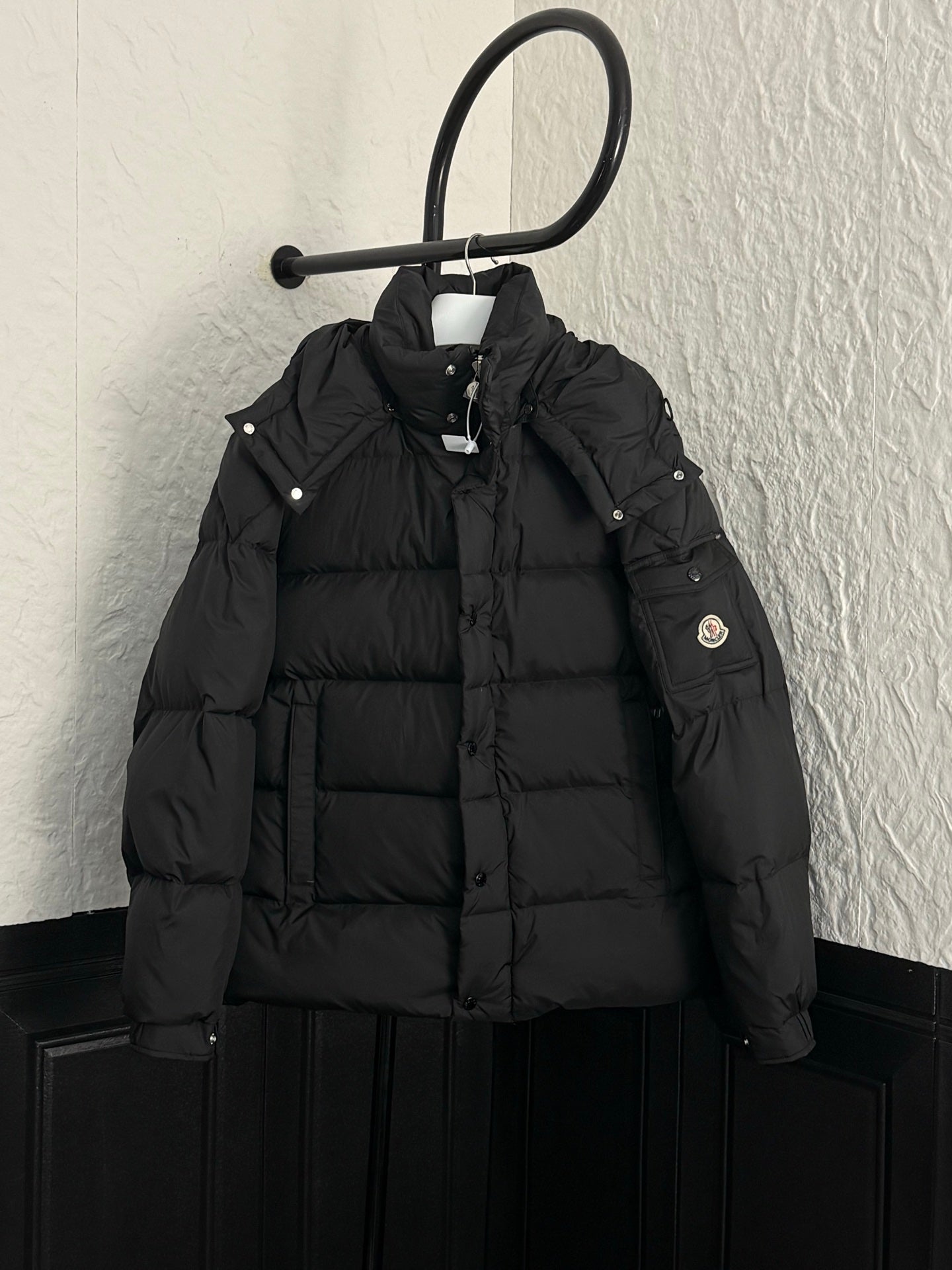Long black puffer jacket with hood, snap buttons, and Moncler chest patch