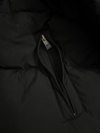 Long puffer coat side pocket zipper with metal pull tab on dark fabric.