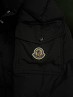 Long puffer coat close-up with Moncler logo patch on chest and button placket.