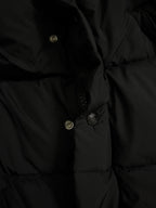 Long puffer coat hood with buttoned placket and metal snaps on dark fabric.