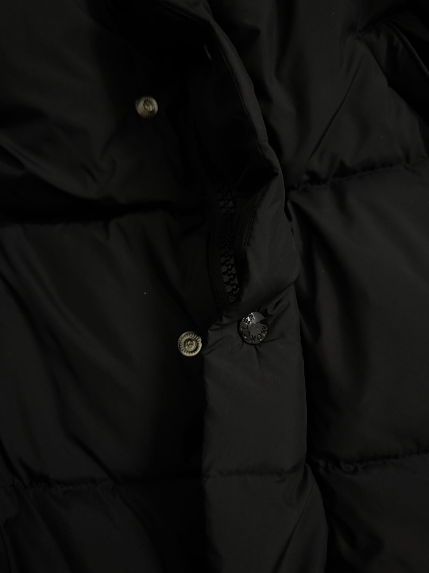 Long puffer coat hood with buttoned placket and metal snaps on dark fabric.