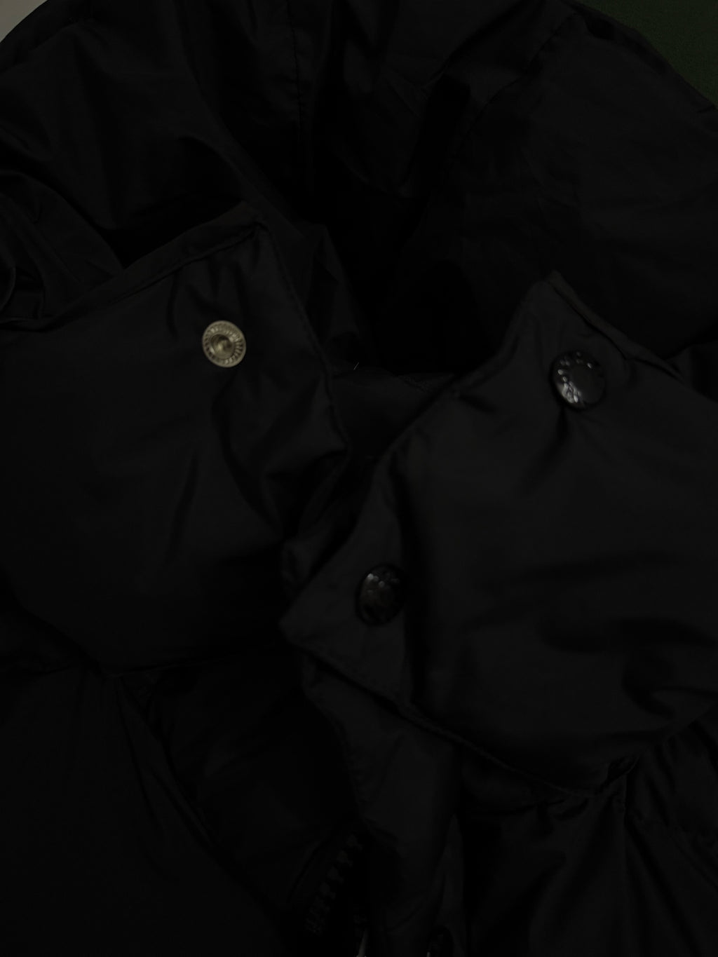 Long puffer coat close-up with metal snap buttons and seam lines on dark fabric.