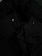 Long puffer coat close-up with metal snap buttons and seam lines on dark fabric.