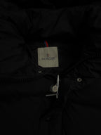 Long puffer coat interior brand label and zipper placket detail, dark fabric.
