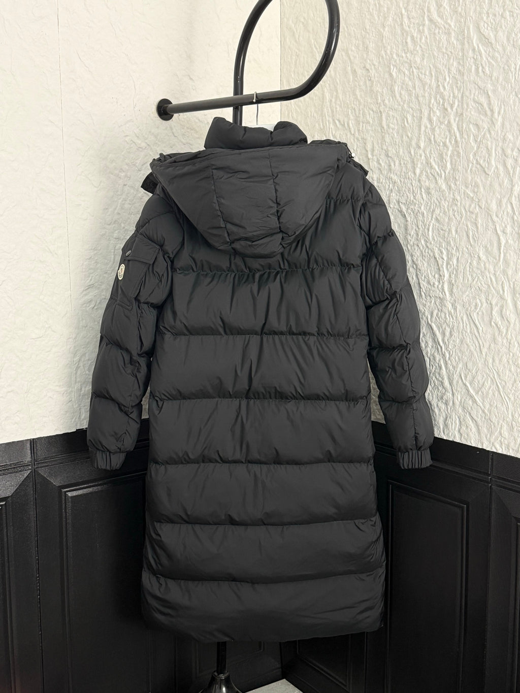 Back view long puffer coat with hood, dark fabric, quilted horizontal panels.