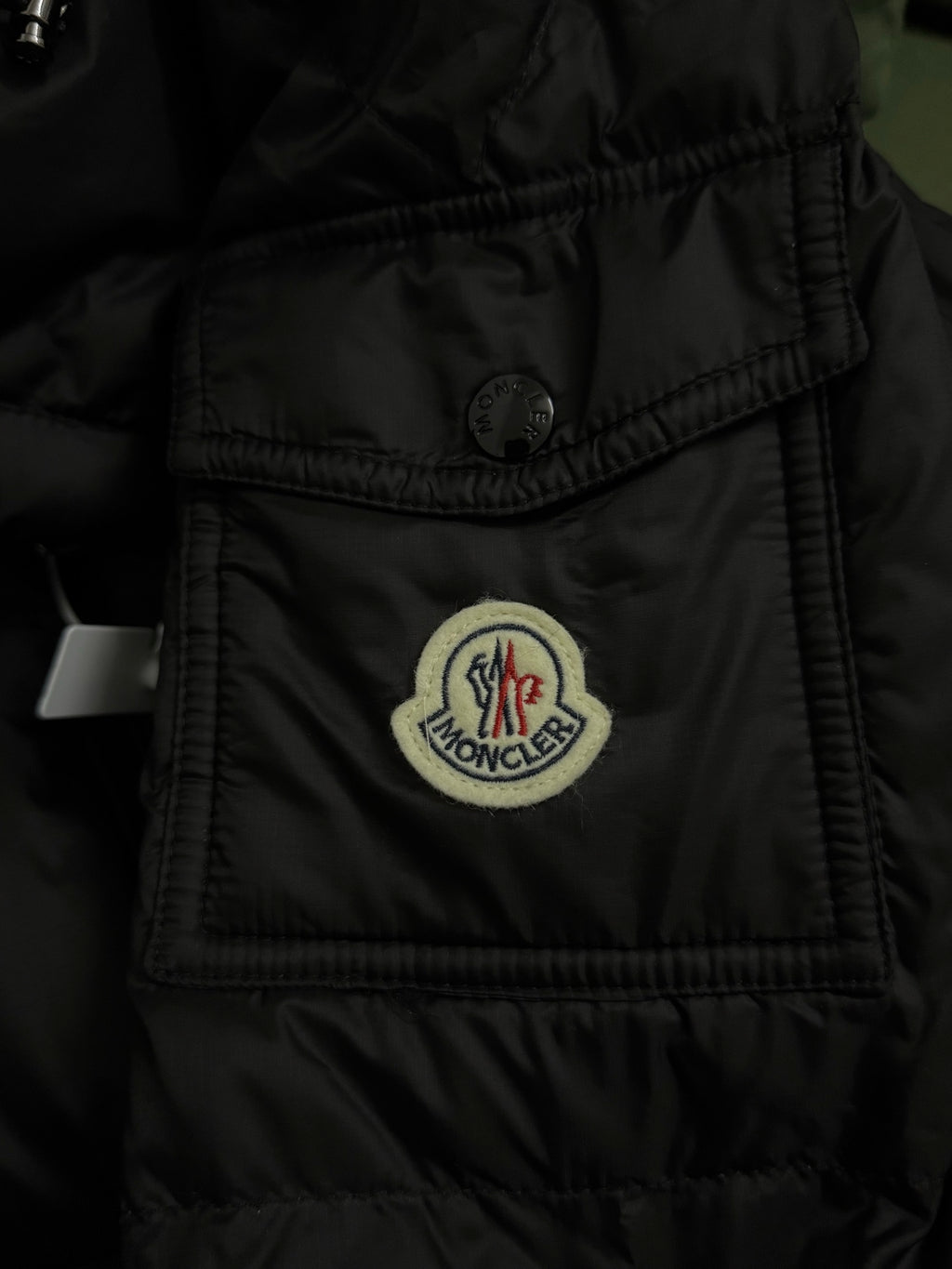 Black puffer jacket chest pocket with Moncler crest patch