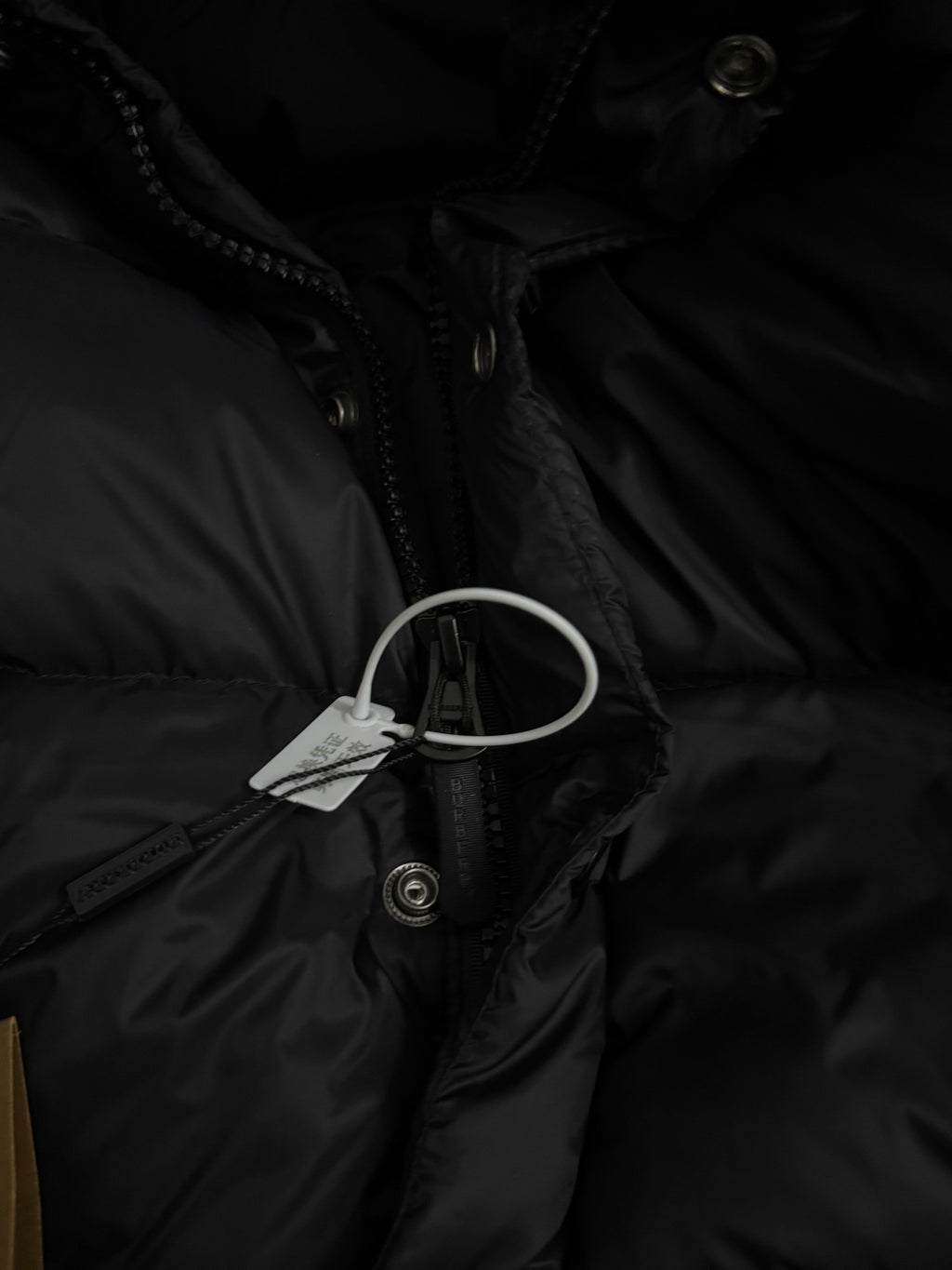 Black puffer jacket with zip front, hood drawstrings, and hanging tag