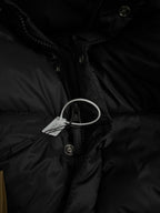 Black puffer jacket with zip front, hood drawstrings, and hanging tag