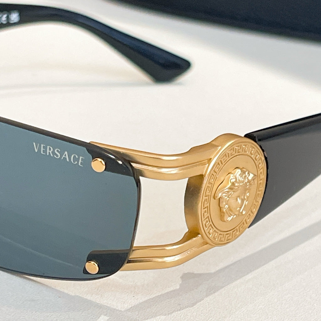 Gold-frame sunglasses close-up with dark blue lenses and engraved medallion